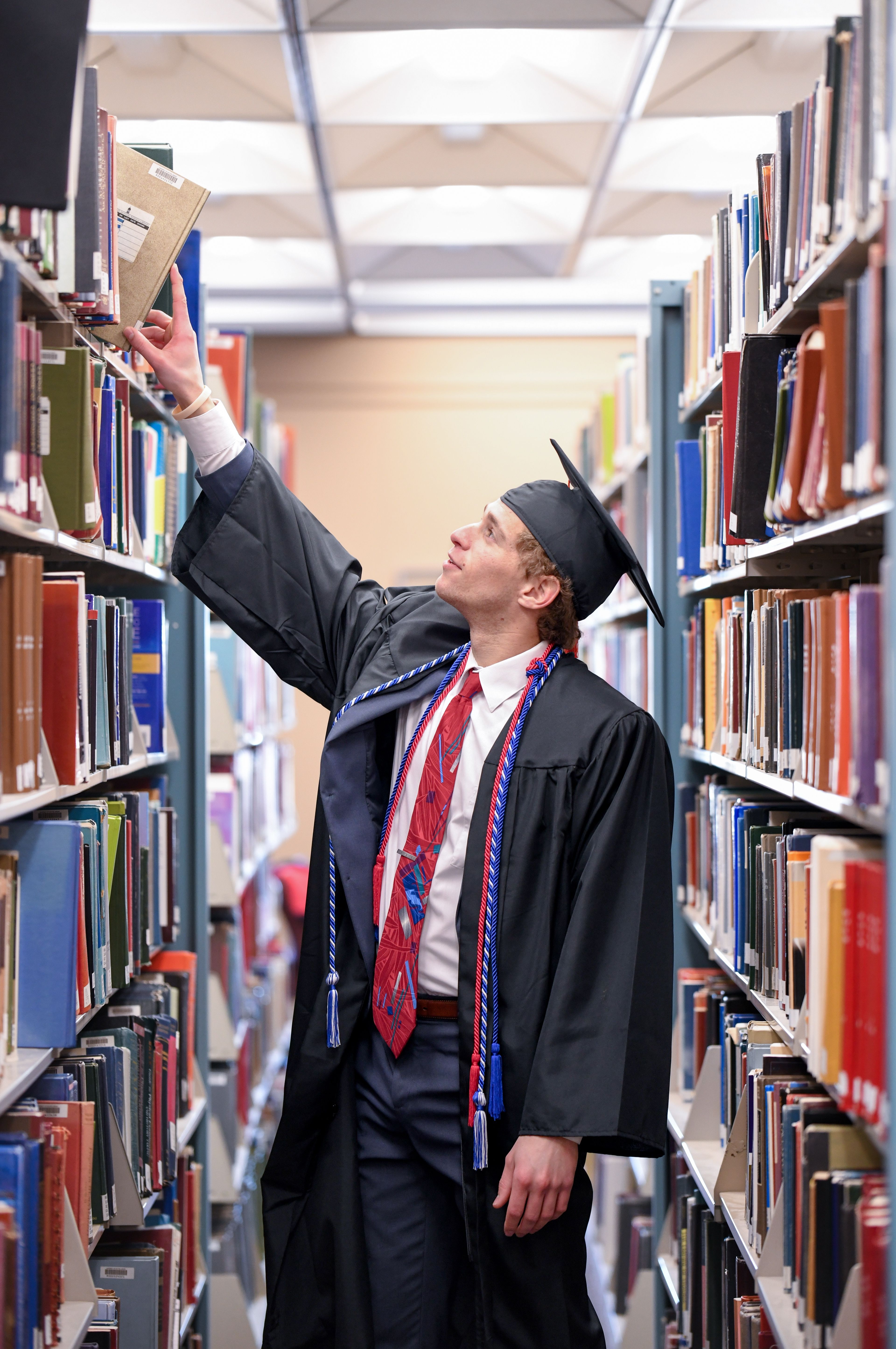 Graduation portrait reaching for book in library